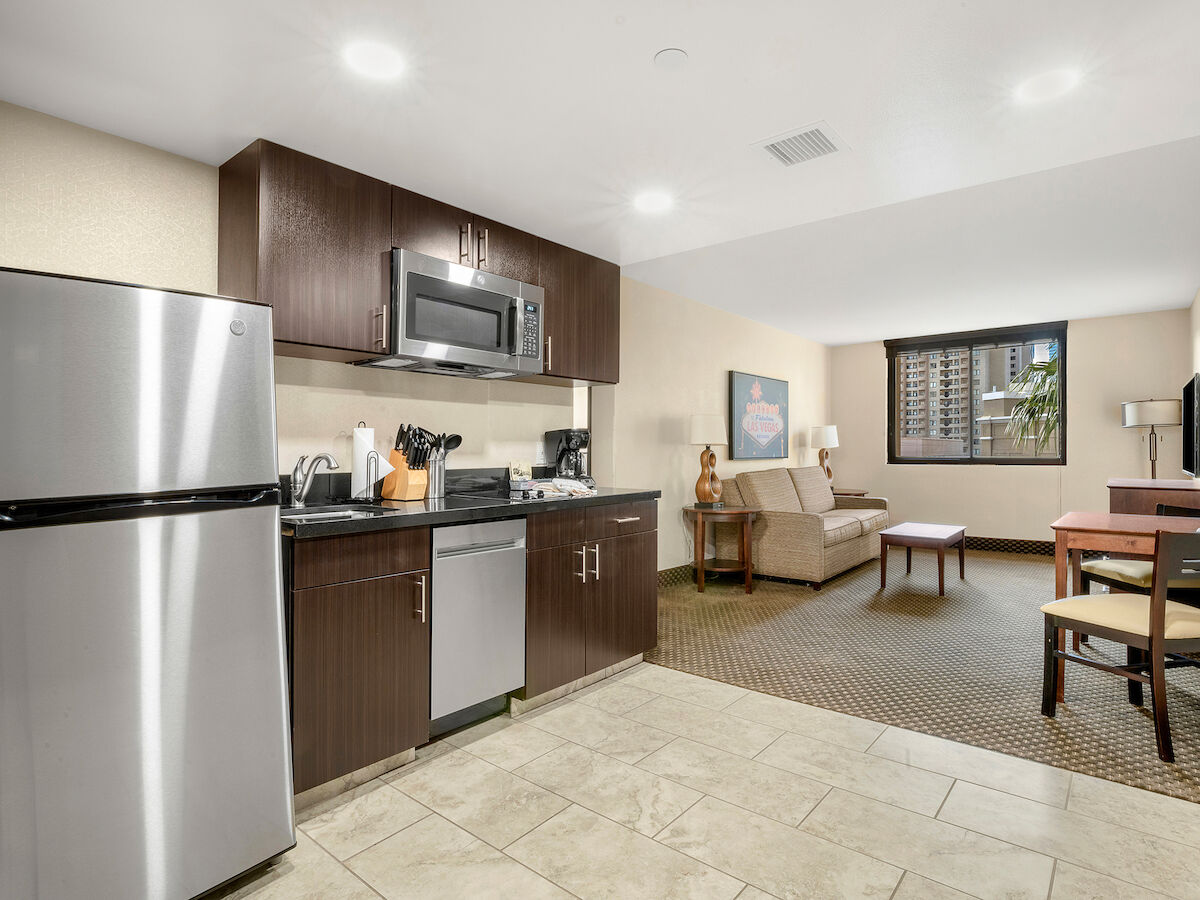 A modern studio apartment features a kitchenette with stainless steel appliances, a living area with a sofa, a TV, and a small dining table.