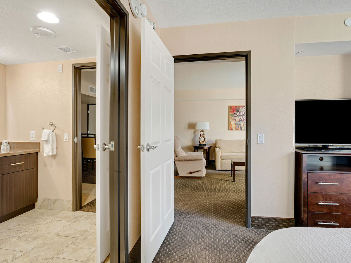 The image shows the interior of a hotel room with a bathroom, a living area, a television, and furniture.