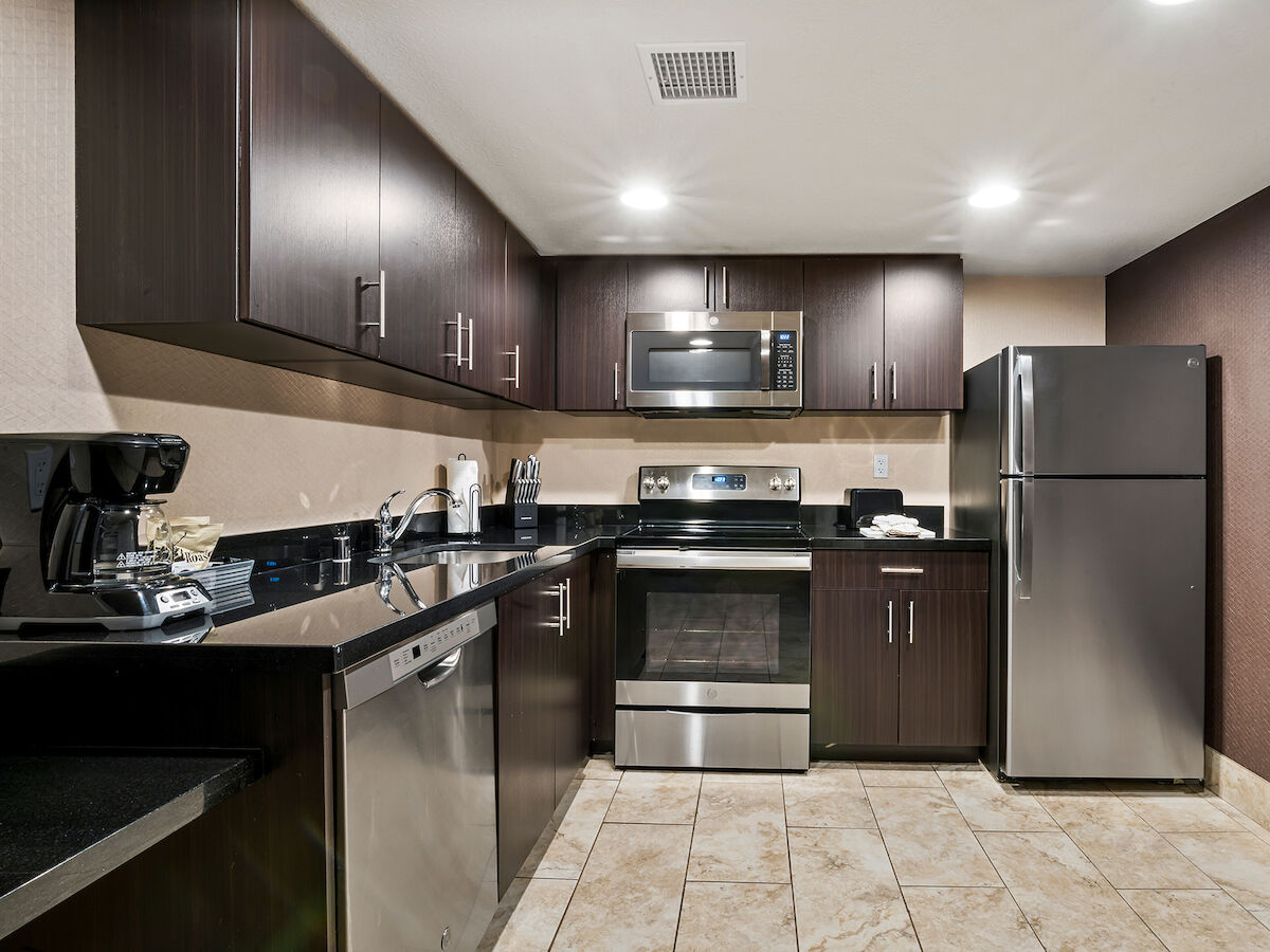 A modern kitchen with dark wood cabinets, stainless steel appliances including a refrigerator, oven, microwave, dishwasher, and a coffee maker on the counter.