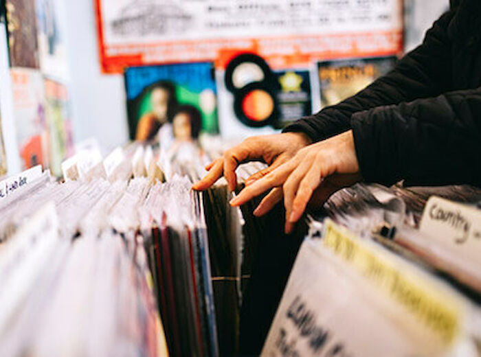 Hands flipping through vinyl records in a store with posters on the wall in the background.