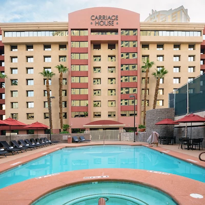This image shows an outdoor pool area with lounge chairs and umbrellas, in front of a building with the sign "Carriage House" on it.