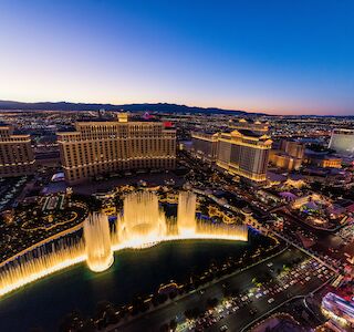 Aerial view of Las Vegas at dusk, featuring the famous Bellagio Fountains illuminated among numerous hotels and casinos along the Strip.
