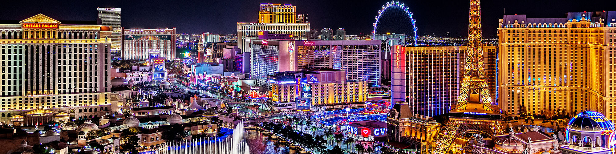This image showcases the vibrant nightlife of the Las Vegas Strip, featuring illuminated hotels, a Ferris wheel, and a large fountain display.